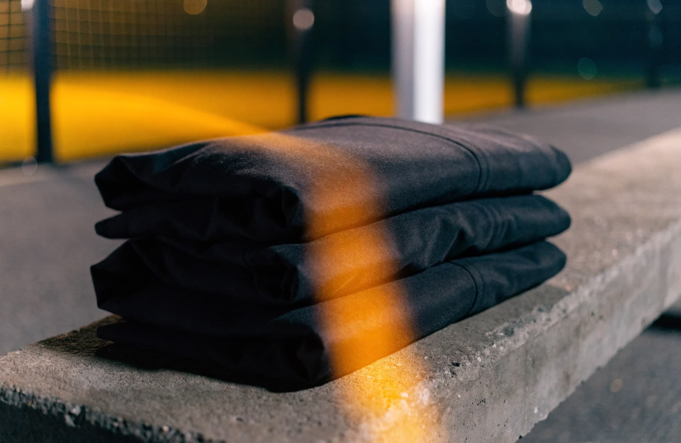 Folded dark garments on a concrete bench beside a padel court at dusk
