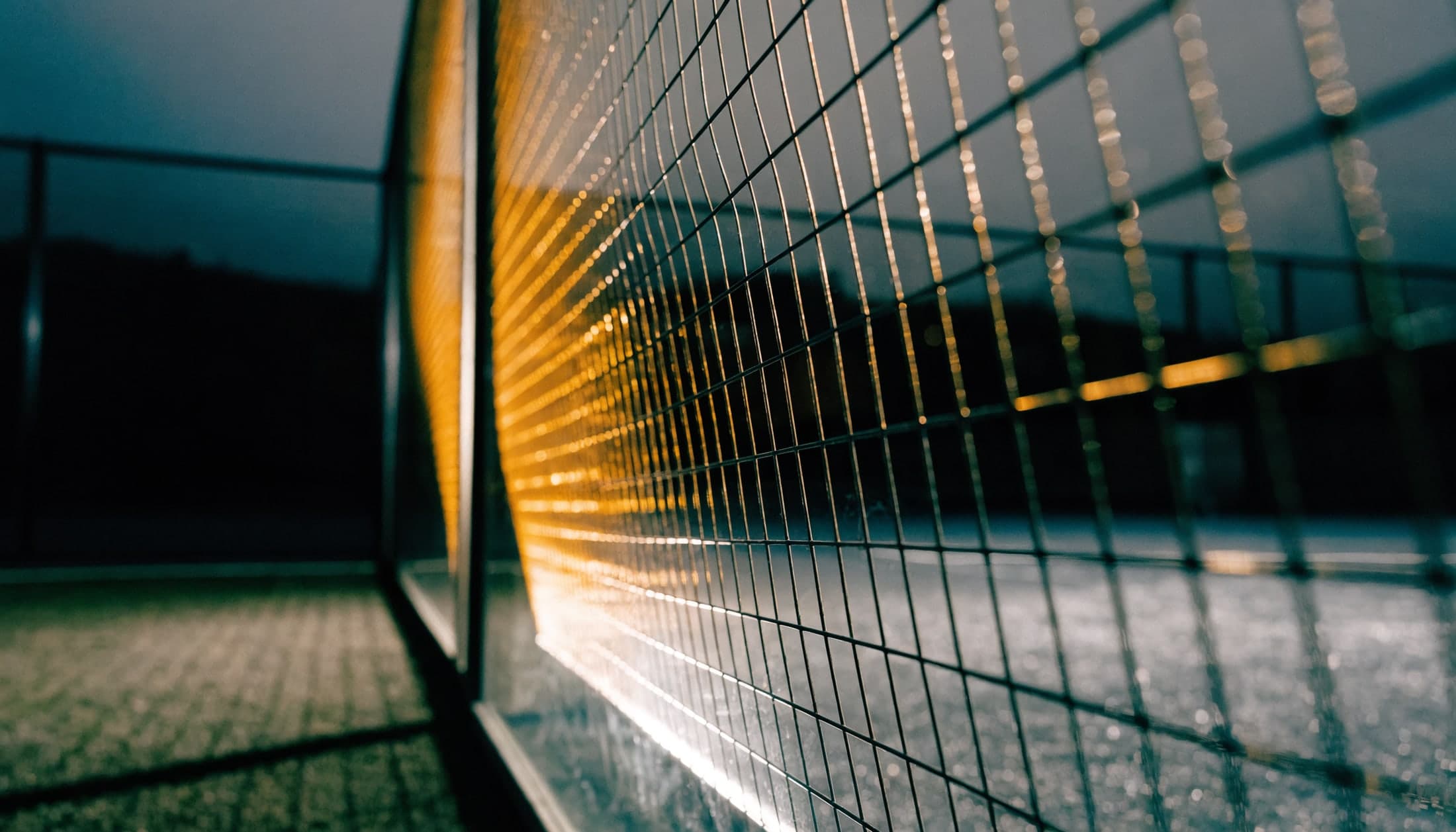Padel court mesh casting grid shadows on dark turf at night